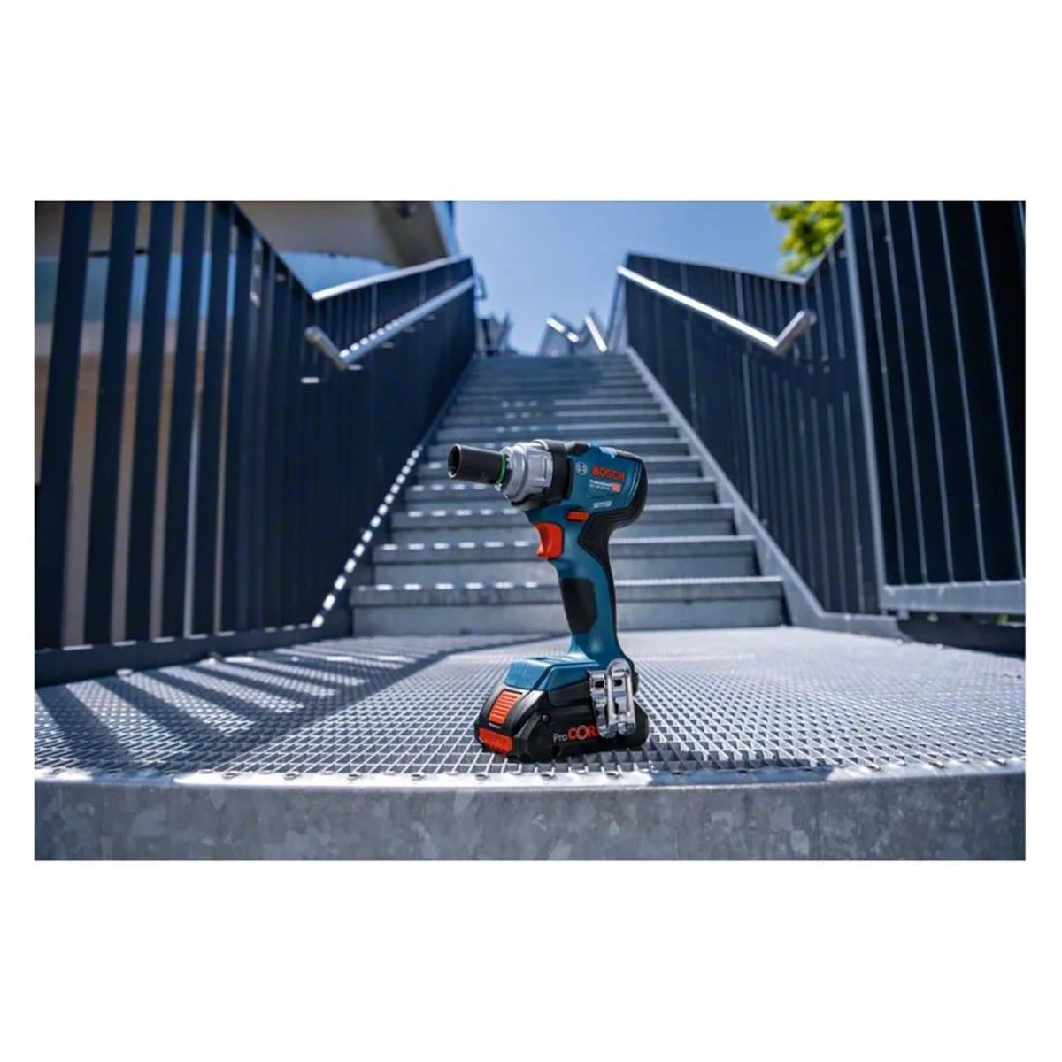 Ein Bosch Professional Akku-Drehschlagschrauber GDS 18V-330 HC steht aufrecht auf einem metallenen Treppenpodest, im Hintergrund erheben sich Außentreppen und Geländer unter einem strahlend blauen Himmel.