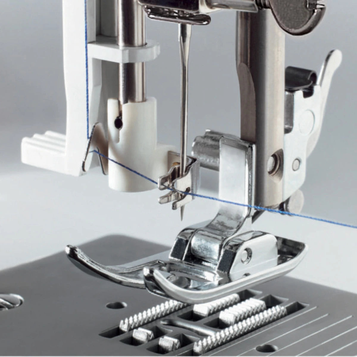 Nahaufnahme der CARINA Power Stretch II Nadel, des Nähfußes und des blauen Fadens mit Einfädelmechanismus und Metalltransporteur - perfekt für Overlockstiche auf elastischen Stoffen.