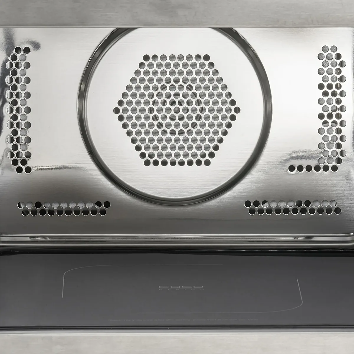 Nahaufnahme der CASO HCMG 25 Mikrowelle - silber interior: 25-Liter-Garraum aus Edelstahl mit sechseckigen Lüftungsschlitzen und Perforationen für die Luftzirkulation, ideal für eine verbesserte Heißluftfunktion. Die Backofentür ist unten teilweise geöffnet. Marke: CASO.