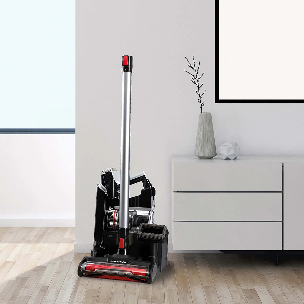 Der INVICTUS X9 Akkustaubsauger in Schwarz steht neben einer weißen Kommode mit grauer Vase und Deko - perfekt für moderne Räume dank HEPA-Filter.