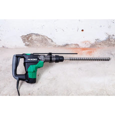 Ein grün-schwarzer Hikoki Bohr- und Meisselhammer DH40MCWSZ SDS-Max mit einem langen Meissel steht an einer Betonwand.