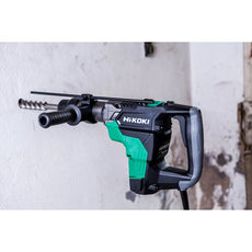 Ein grüner und schwarzer Hikoki Bohr- und Meisselhammer DH40MCWSZ SDS-Max ist einsatzbereit an einer weißen Wand montiert.