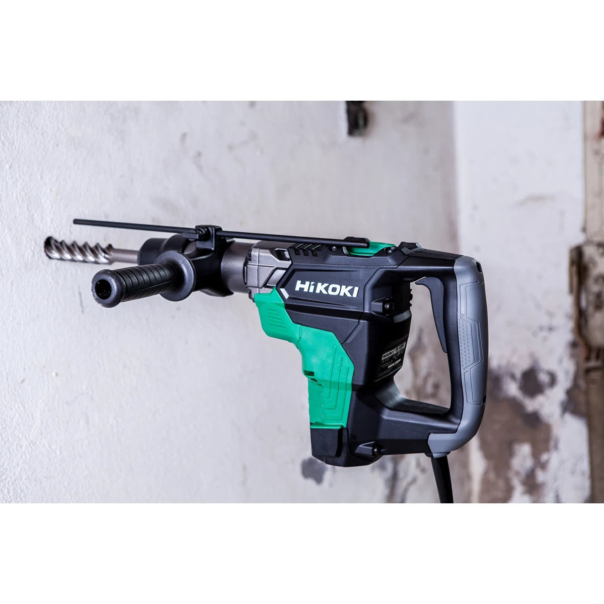 Ein grüner und schwarzer Hikoki Bohr- und Meisselhammer DH40MCWSZ SDS-Max ist einsatzbereit an einer weißen Wand montiert.