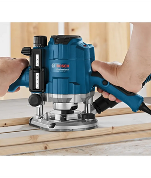 Hände, die eine blaue Bosch Oberfräse Holzfräse GOF 1250 CE mit präziser Tiefeneinstellung auf Holzbrettern in einer Werkstattumgebung bedienen.