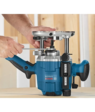 Eine Person stellt die Bosch Oberfräse Holzfräse GOF 1250 CE mit einem Schraubenschlüssel auf einer hölzernen Unterlage in einer Werkstatt ein und konzentriert sich dabei auf die präzise Frästiefen-Feineinstellung für genaues Fräsen.