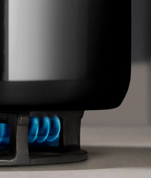 Nahaufnahme eines schwarzen WMF Topfset 4-tlg. Fusiontec Essential Pro Topf auf einem Herd, der von einer blauen Gasflamme erhitzt wird. Dieses 4-teilige Set von WMF aus langlebigem Fusiontec-Material garantiert zuverlässige Leistung beim täglichen Kochen.