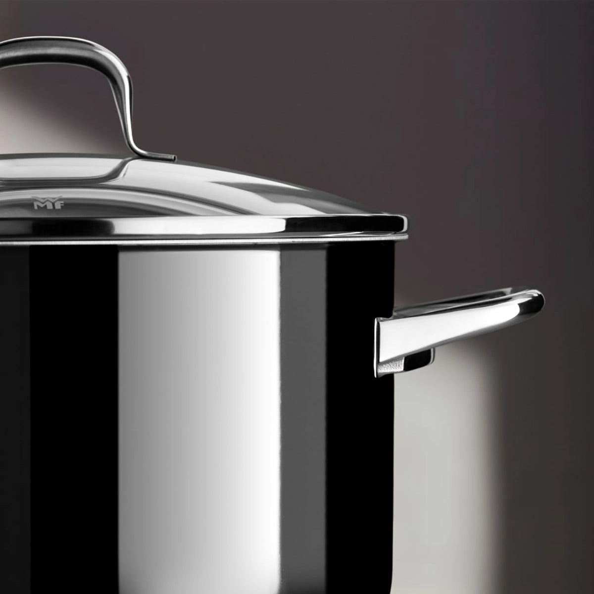 Eine Nahaufnahme des WMF Topfset 4-tlg. Fusiontec Essential Pro, einem glänzend schwarz-silbernen Kochtopf mit Deckel und Griff von WMF, hergestellt aus dem langlebigen Fusiontec-Material, vor einem dunklen Hintergrund.