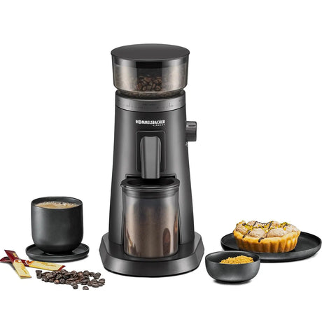 Die ROMMELSBACHER EKM 600 Kaffeemühle in Schwarz ist auf dem Tisch zusammen mit Kaffeebohnen, einer Tasse Kaffee, einem Stück Torte und Zucker abgebildet. Diese hochwertige Kaffeemühle von ROMMELSBACHER verfügt über ein Edelstahl-Kegelmahlwerk und mehrere Mahlstufen, die jedes Mal für perfekt gemahlenen Kaffee sorgen.
