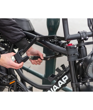 Eine Person sichert ein schwarzes WAAP E-Bike mit dem ABUS Faltschloss Bordo Granit 6500K an einem Pfosten und hält dabei den Schlüssel in der Hand.