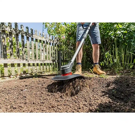 Eine Person bearbeitet die Gartenerde an einem Holzzaun und Grünpflanzen mit der AL-KO TLD 1820 Akku-Bodenhacke - schwarz und genießt die kabellose Bodenbearbeitung mit dem starken AL-KO 18V Akku an einem sonnigen Tag.