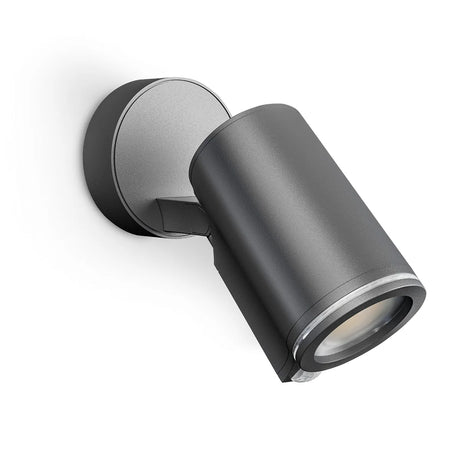 Schwarze, zylindrische Außenwandleuchte mit runder Montageplatte vor weißem Hintergrund im Design des Steinel STEINEL Spot ONE S LED-Außenstrahlers – schwarz – und integriertem Bewegungsmelder für mehr Sicherheit.