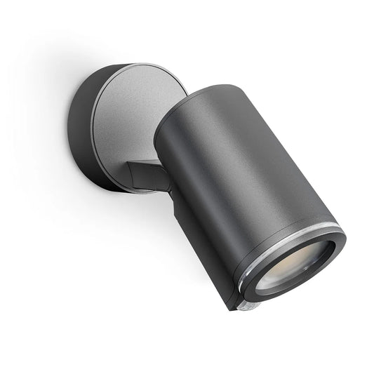 Schwarze, zylindrische Außenwandleuchte mit runder Montageplatte vor weißem Hintergrund im Design des Steinel STEINEL Spot ONE S LED-Außenstrahlers – schwarz – und integriertem Bewegungsmelder für mehr Sicherheit.