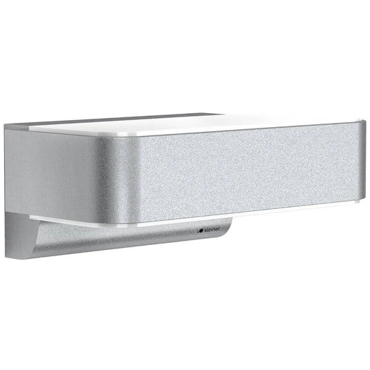 Die STEINEL L 810 SC Sensor-Außenleuchte von Steinel ist eine moderne, silberfarbene, rechteckige Wandleuchte mit einem schlichten, minimalistischen Design, die vor einem weißen Hintergrund für eine elegante Fassadenbeleuchtung sorgt.
