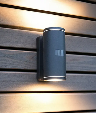Die Steinel L 940 SC Außenwandleuchte von Steinel ist eine moderne, an der Wand montierte LED-Außenleuchte in Schwarz, die sowohl nach oben als auch nach unten auf horizontale Holzlamellen strahlt und Ihrem Außenbereich Stil und Funktionalität verleiht.