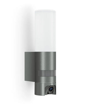 Die STEINEL L 625 CAM SC Außen-Wandleuchte von Steinel in Silber ist eine moderne Zylinderleuchte zur Wandmontage mit integrierter Überwachungskamera am unteren Ende.