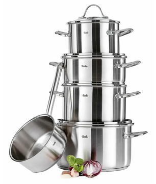 Das Fissler Topf-Set PARIS 5-teilig von Fissler aus Edelstahl ist gestapelt mit Deckeln arrangiert, daneben stehen eine induktionsgeeignete Stielkasserolle sowie Zwiebel, Knoblauch und Minze.