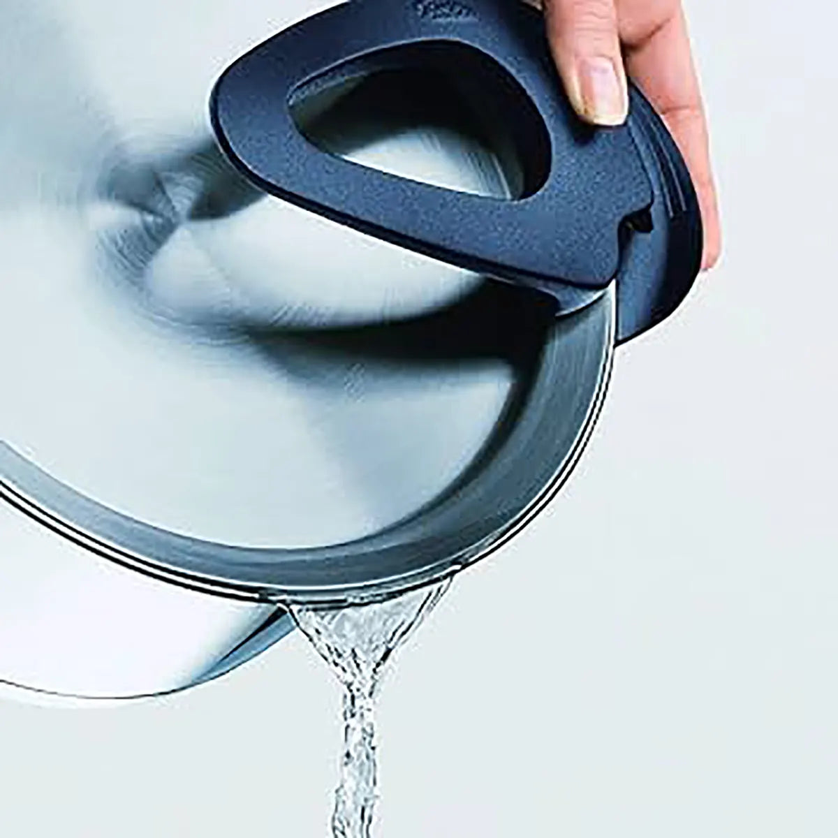 Eine Hand gießt Wasser durch den eingebauten Siebdeckel eines Fissler Topfset Intensa 5-tlg. matt-praktisch und induktionsgeeignet.