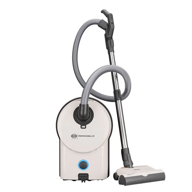 Der SEBO Professional D9 Bodenstaubsauger in Weiß verfügt über einen grauen Schlauch und einen Metallstiel und steht aufrecht vor einem weißen Hintergrund – ideal für eine effektive Teppichreinigung.