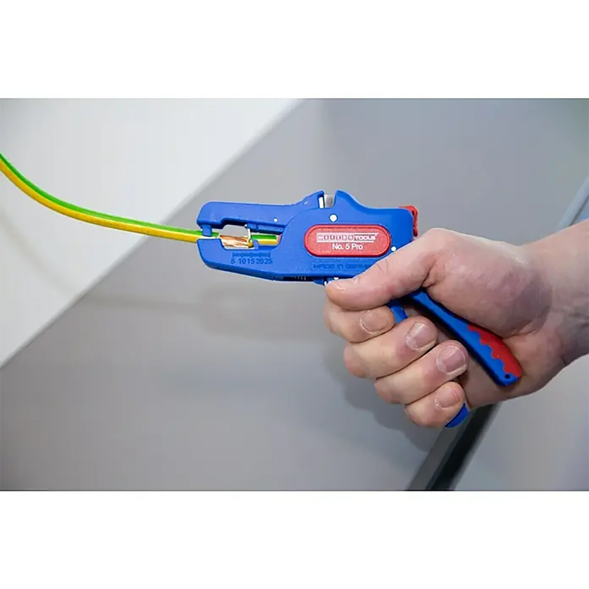 Eine Hand benutzt die Weicon No. 5 Pro Abisolierzange - blau von Weicon zum Abisolieren eines gelb-grünen Drahtes und bietet damit Präzision für Elektroinstallationen.