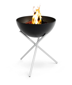 Die Höfats BOWL 57 Feuerschale - schwarz ist eine moderne schwarze Feuerschale von Höfats mit gekreuzten silbernen Metallbeinen und lebendigen Flammen auf weißem Hintergrund.