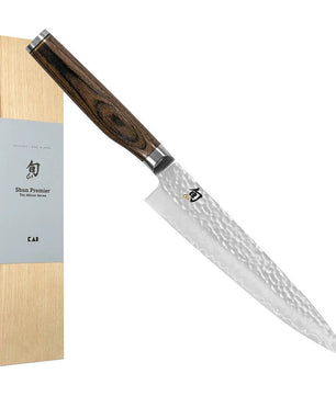 Das KAI Shun TDM-1701 Premier Tim Mälzer Allzweckmesser – braun verfügt über eine Klinge aus gehämmertem Damaszenerstahl und einen braunen Holzgriff und wird neben seiner hellen Holzbox präsentiert.