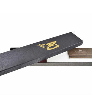 Eine rechteckige schwarze Geschenkbox mit goldener Beschriftung, die teilweise geöffnet ist, um eine Karte und das weiße Innere zu präsentieren – eine elegante Verpackung für das KAI Shun DM-0728 Nakiri von KAI.
