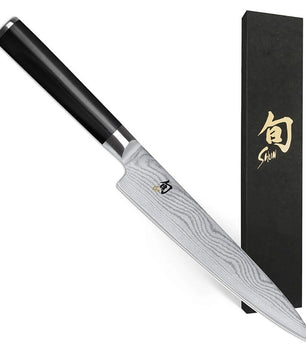 Ein KAI Shun DM-0701 Allzweckmesser von KAI mit braunem Griff und Damastklinge liegt neben einer schwarzen Schachtel mit goldener japanischer Schrift.