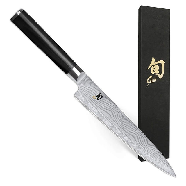 Ein KAI Shun DM-0701 Allzweckmesser von KAI mit braunem Griff und Damastklinge liegt neben einer schwarzen Schachtel mit goldener japanischer Schrift.