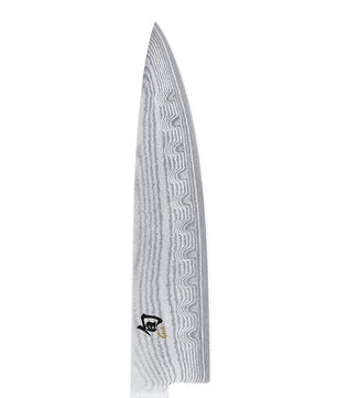 Das KAI DM-0719 Shun Kochmesser – schwarz verfügt über eine gemusterte Damaszener-Klinge und ein kleines schwarz-goldenes Emblem nahe des Griffs, das dem Messer eine elegante Note verleiht.