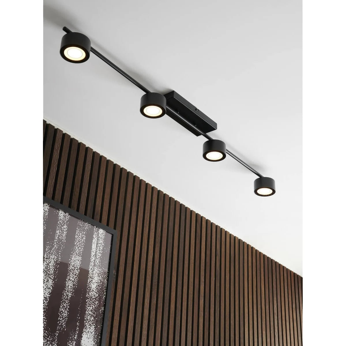 Die Nordlux Clyde Deckenleuchte in schwarz von Nordlux verfügt über vier verstellbare runde Strahler im skandinavischen Design, die sich ideal für die Montage über vertikalen Holzlatten und einem schwarz gerahmten abstrakten Kunstwerk eignen.