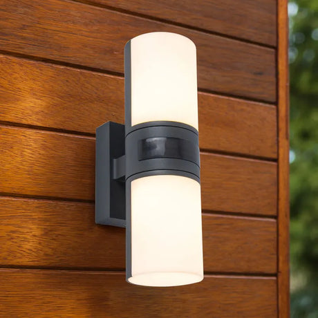 Die Lutec Cyra Wandleuchte - grau von Lutec ist eine moderne zylindrische LED-Außenwandleuchte mit mattiertem Glas, ideal für die stilvolle Außenbeleuchtung von Holzverkleidungen im Außenbereich.
