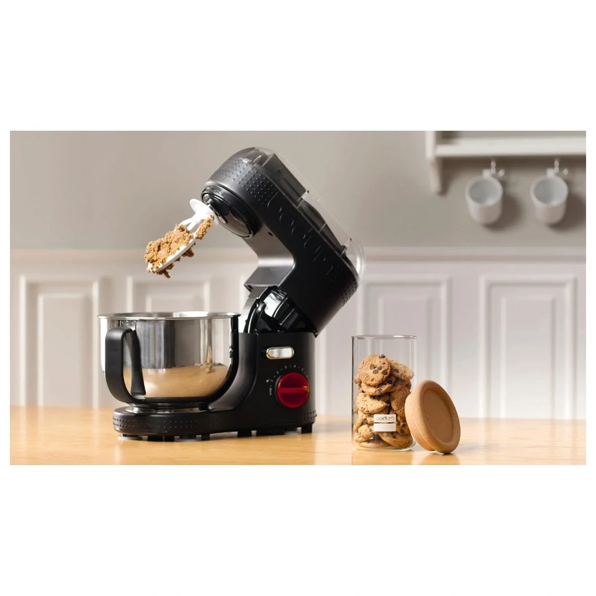 Die Bodum Bistro 11381 Küchenmaschine in Schwarz mit starkem 700-Watt-Motor steht im Retro-Design auf der Arbeitsplatte neben einem Glas Cookies, während frischer Keksteig am Aufsatz haftet.
