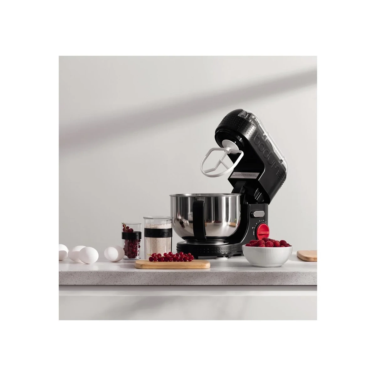 Die Bodum Bistro 11381 Küchenmaschine - Schwarz mit Metallschüssel steht auf der Theke zwischen Eiern, Beeren und Gläsern - ihr Retro-Design und der 700-Watt-Motor vereinen Stil und Effizienz bei jeder Küchenarbeit.