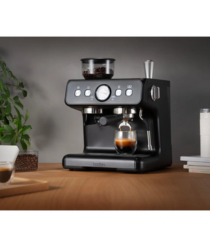 Die Bodum Bistro 12459-01 Espressomaschine in Schwarz von Bodum bereitet aromatischen Espresso auf einer Holztheke zu - umgeben von Kaffeebohnen, Tassen und einer Pflanze, ideal für frisch gebrühten Espresso und feinen Milchschaum.