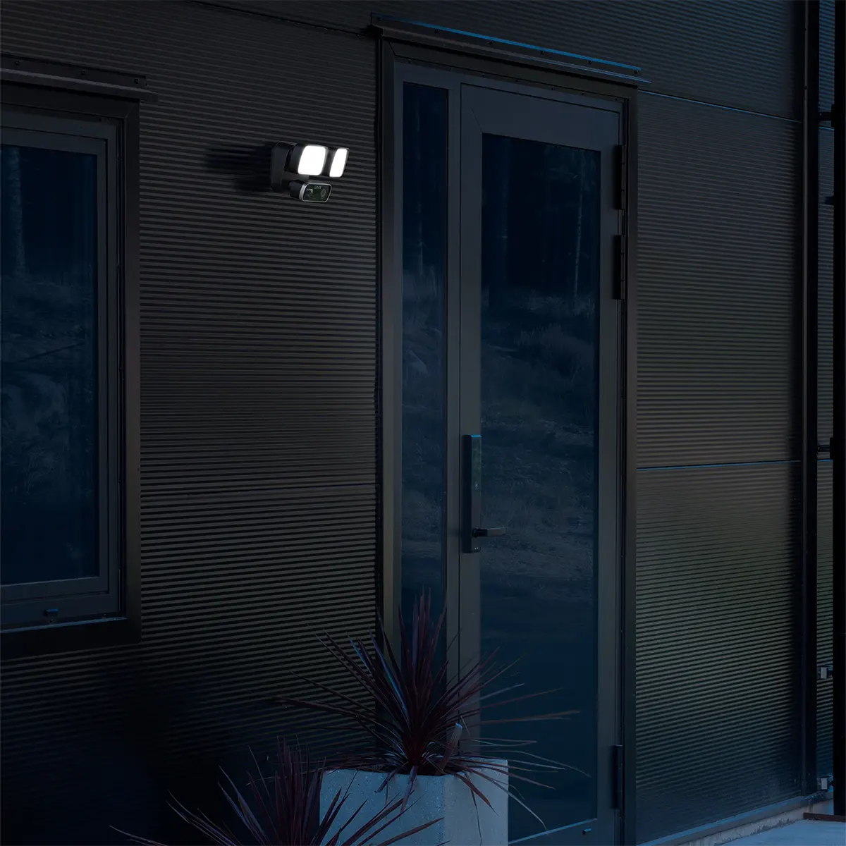 Eine moderne Außentür bei Nacht, beleuchtet von der Konstsmide Smartlight 7869-750 Kameraleuchte in schwarz, für mehr Sicherheit und Sichtbarkeit.