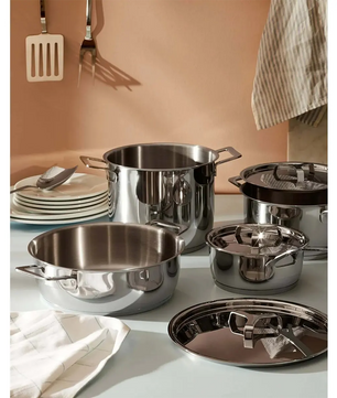 Das Alessi AJM100S9 9er-Set Stahltöpfe in silber, induktionsgeeignet, steht auf einer Küchentheke mit an der Wand hängenden Utensilien.