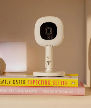 Ein Nanit Pro mit Flex-Ständer Babyphone in Weiß von Nanit steht auf zwei Parenting-Büchern im Regal.