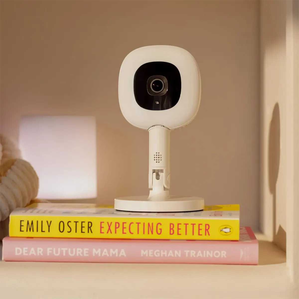 Ein Nanit Pro mit Flex-Ständer Babyphone in Weiß von Nanit steht auf zwei Parenting-Büchern im Regal.