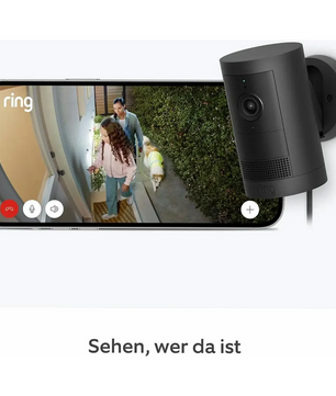 Eine „Ring Außenkamera Plus Akku – schwarz“ von Ring zeigt ein gestochen scharfes Bild in 2K-Auflösung von einem Paar und ihrem Hund vor der Haustür und demonstriert damit die Bildschärfe dieser kabellosen Überwachungskamera.