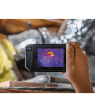 Eine Hand hält eine Seek Thermal SHOT PRO Wärmebildkamera von Seek Thermal in Schwarz, die die Wärmesignaturen von Objekten in einem Dachgeschoss aufnimmt.