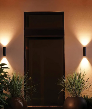 Moderner Eingangsbereich mit intelligenter Außenbeleuchtung - zwei Philips Hue Outdoor Appear Wandleuchten - Schwarz von Philips erhellen den Eingangsbereich, mit Topfpflanzen auf jeder Seite.