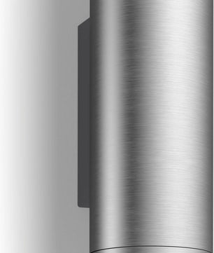 Eine zylindrische Wandleuchte aus gebürstetem Metall, wie beispielsweise die „Philips Hue Appear Ambiance Außenwandleuchte“ in Silber von Philips, wirft einen auffälligen Schatten auf eine weiße Wand – ideal, um Ihre Smart-Home-Beleuchtung aufzuwerten.