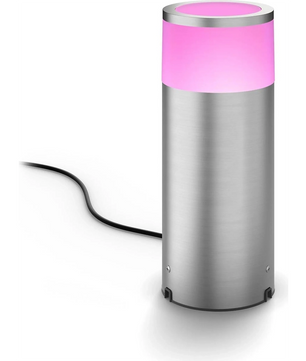 Die Philips Hue Calla Ambiance Sockelleuchte – schwarz von Philips ist eine zylindrische Lampe aus Edelstahl mit einem rosa leuchtenden Oberteil und einem dahinter herhängenden schwarzen Netzkabel. Sie sorgt in jedem Außenbereich für stilvolle und intelligente Gartenbeleuchtung.
