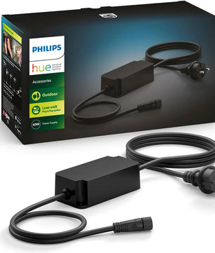 Das Philips Hue Outdoor-Netzteil – schwarz von Philips mit IP67-Zertifizierung bietet zuverlässigen Schutz vor Wasser und Staub und ist die perfekte Ergänzung für Ihr Niedervolt-Außenbeleuchtungssystem. Im Hintergrund sind das Anschlusskabel, der Stecker und die Produktverpackung zu erkennen.