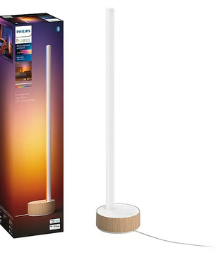 Die hohe, schlanke Tischleuchte „Philips Hue Gradient Signe“ – weiß von Philips mit Holzsockel steht neben ihrer Verpackung in Sonnenuntergangsfarben und verfügt über die innovative Gradient-Technologie für eine intelligente Lichtsteuerung.