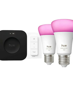 Zwei Philips Hue A60 E27 LED-Lampen mit rosa Licht, ein schwarzer Hub und ein weißer Wandschalter vor weißem Hintergrund – das perfekte smarte Beleuchtungserlebnis als Teil des Philips Hue A60 E27 Starter-Kits V3 von Philips.