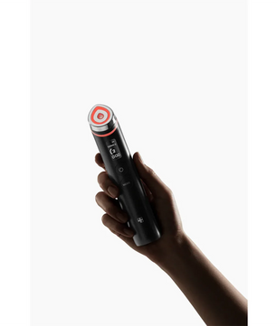 Eine Hand hält den Medicube Age-R Booster Pro von Medicube, ein schwarzes Anti-Aging-Gerät mit einem roten Ring um die runde Spitze, das die Elastizität der Haut verbessern soll, vor einem weißen Hintergrund.