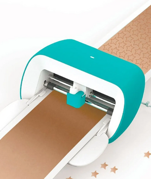 Der Cricut Joy Schneideplotter in türkis/weiß von Cricut schneidet Sternformen auf braunes Papier - ideal für kreative DIY-Projekte.