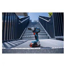 Ein Bosch Professional Akku-Drehschlagschrauber GDS 18V-330 HC steht aufrecht auf einem metallenen Treppenpodest, im Hintergrund erheben sich Außentreppen und Geländer unter einem strahlend blauen Himmel.