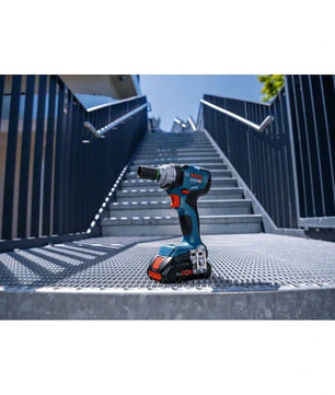 Ein Bosch Professional Akku-Drehschlagschrauber GDS 18V-330 HC steht aufrecht auf einem metallenen Treppenpodest, im Hintergrund erheben sich Außentreppen und Geländer unter einem strahlend blauen Himmel.